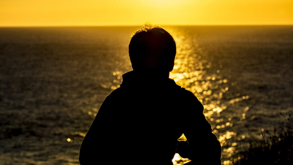 Silhouette of a teenager boy looking at the sea on sunset